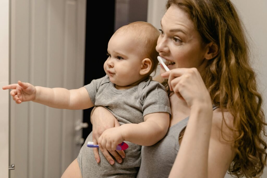 pexels-photo-7491269-7491269 Close-Up Photo of a Mother Carrying Her Baby while Brushing Her Teeth