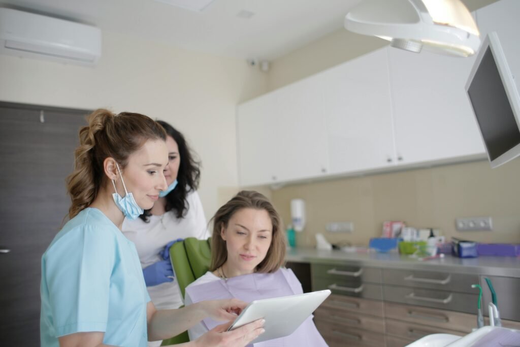 pexels-photo-3952136-3952136 Dental professionals engage with a patient using a tablet in a clinical setting, showcasing teamwork and care.
